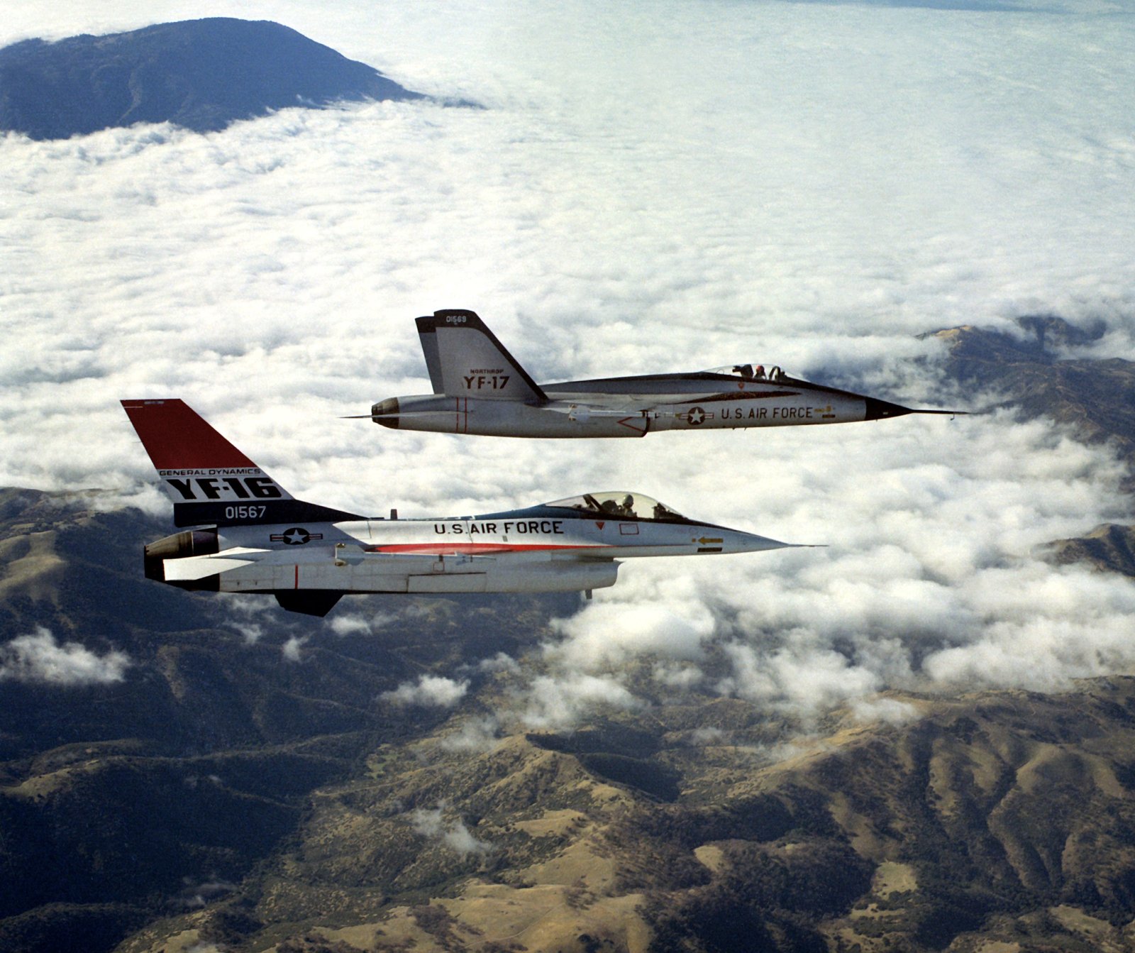 The General Dynamics YF-16 and the Northrop YF-17 prototypes flying in formation above clouds and mountains